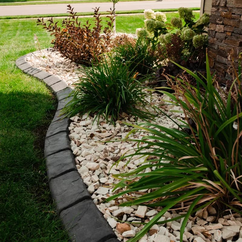 Stamped dark concrete curbing with decorative plantings and stone wall by ATK Landscaping