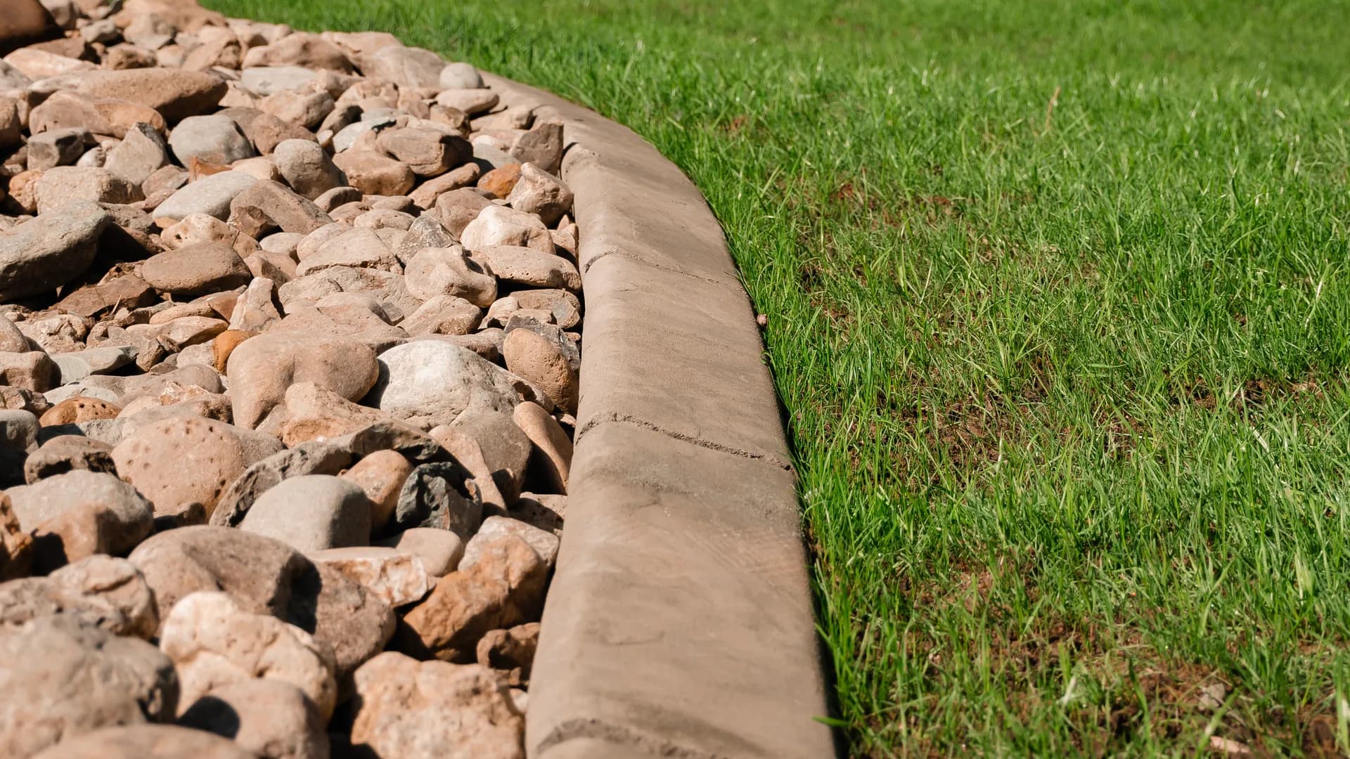Close-up of finished concrete landscape curbing with rock bed and evergreen trees by ATK Landscaping