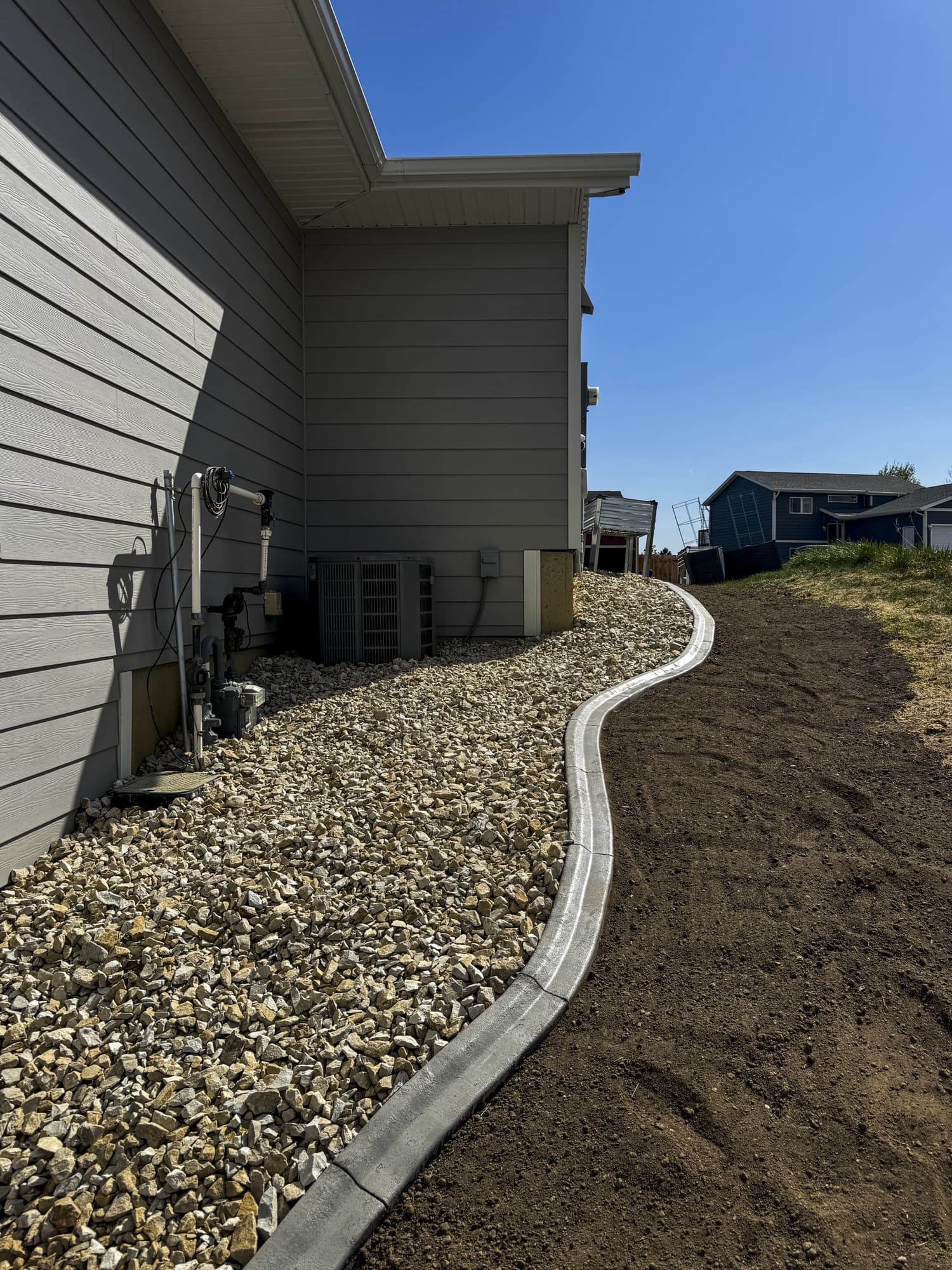 Curved curbing beside a rock bed along a gray house