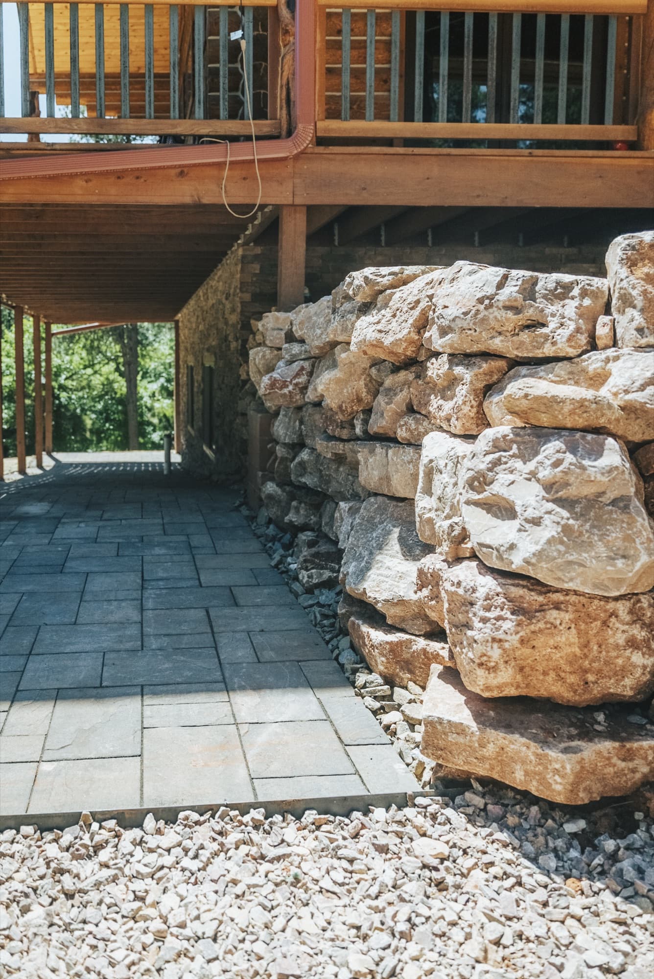 Rectangular pavers beside a large rock wall beneath a deck