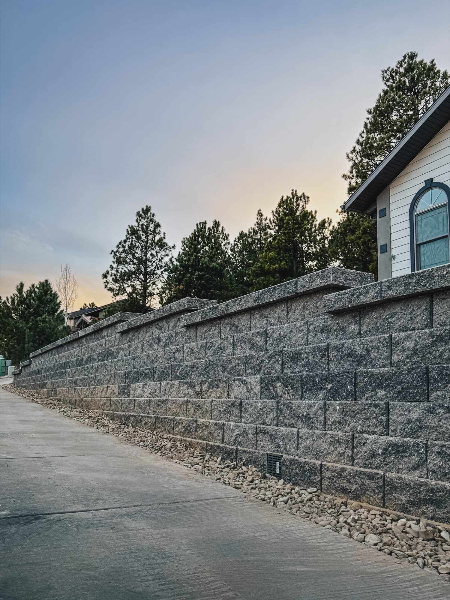 Block retaining wall along a sidewalk beside a white building